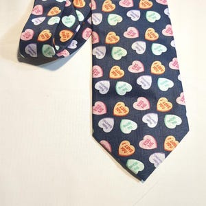 May include: A navy blue tie patterned with colourful candy hearts, each bearing a different message. Phrases like "Kiss Me" and "I Love You" are visible. A classic accessory.