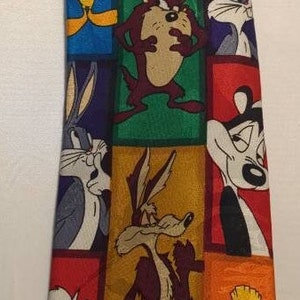 Puede incluir: Una corbata de seda colorida con varios personajes de dibujos animados de Looney Tunes, incluyendo Bugs Bunny, Piolín, el Coyote y el Correcaminos.