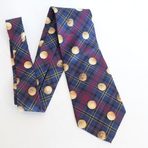 May include: A blue, burgundy, and gold plaid necktie with a repeating pattern of gold circles. The tie is made of a woven fabric and is displayed on a white surface. The tie is a classic accessory.