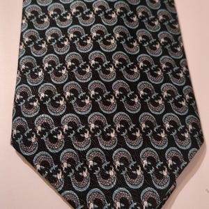 May include: A black necktie with a repeating pattern of stylized, interconnected shapes in light blue, gray, and white. The tie is made of a smooth fabric and has a classic pointed end.