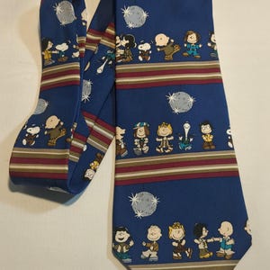 May include: A blue silk tie featuring a repeating pattern of the Peanuts characters dancing with disco balls. The tie has red, white and brown stripes.