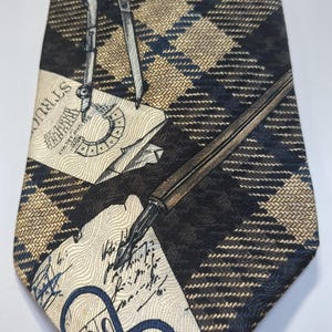 May include: A patterned tie with a repeating plaid design in black, navy, and tan. The tie features illustrations of drafting tools, architectural drawings, and script. The overall theme is architecture and design.