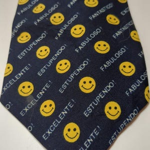 May include: Navy blue necktie with a repeating pattern of yellow smiley faces and phrases like "Excellent!" and "Fabulous!" in white. The tie is a classic accessory for formal or semi-formal attire.