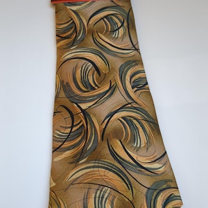 May include: A brown tie with a swirling pattern in shades of tan, gray, and black. The tie has a black band with the text "J. Garcia" in red. The tie is made of a smooth, silky material.