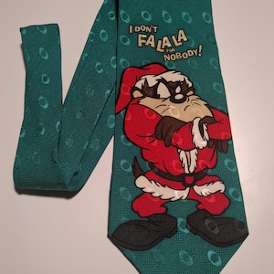 May include: A green tie with a white polka dot pattern. The tie features a cartoon image of a Tasmanian Devil dressed as Santa Claus. The text "I don't falala for nobody!" is printed on the tie.