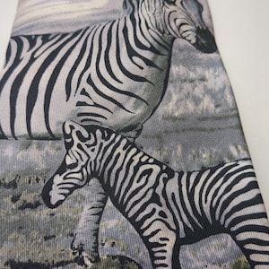 May include: A necktie featuring a detailed illustration of zebras in a natural landscape. The tie showcases a repeating pattern of black and white striped zebras against a muted background of greens, grays, and blues, creating a wildlife theme.