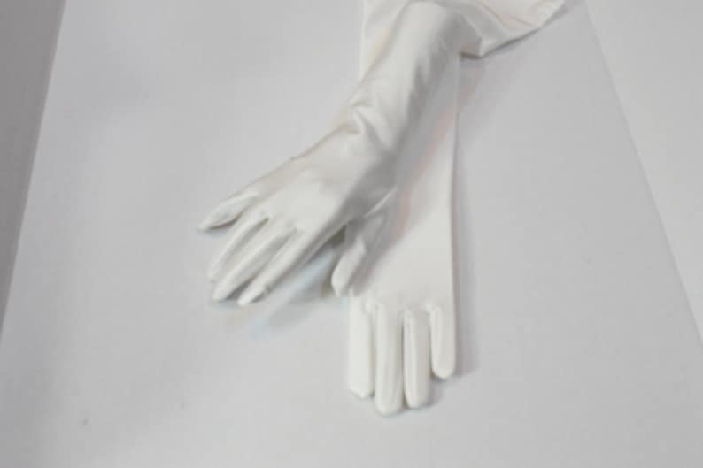 Puede incluir: Un par de guantes largos de sat&eacute;n blanco. Los guantes est&aacute;n doblados por la mitad y las yemas de los dedos se tocan.