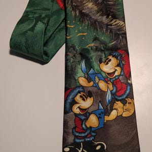 Könnte beinhalten: Eine grün-braune gemusterte Krawatte mit einer Weihnachtsszene mit Mickey Mouse und einem Weihnachtsbaum. Mickey Mouse trägt einen rot-weißen Weihnachtsmann-Anzug und einen blauen Hut.