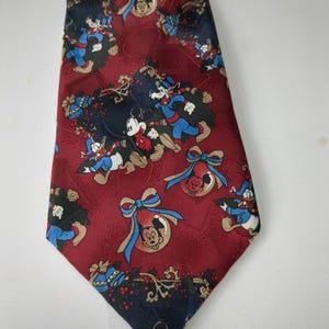 Könnte beinhalten: Eine rote Seidenkrawatte mit Weihnachtsmotiv mit Mickey Mouse, Donald Duck und Goofy. Die Krawatte hat ein sich wiederholendes Muster aus den Figuren und Ornamenten.