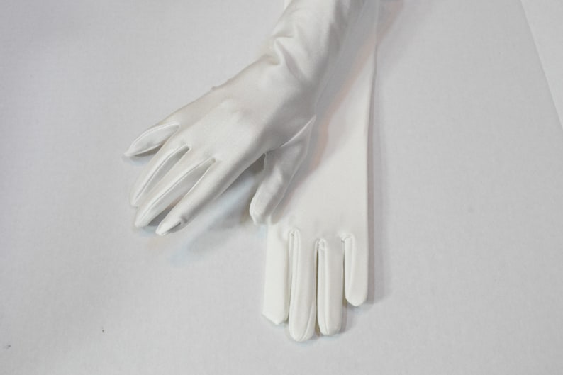 Puede incluir: Un par de guantes de sat&eacute;n blanco, un guante est&aacute; doblado sobre el otro, con las yemas de los dedos de ambos guantes visibles.