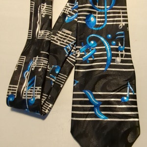 May include: A black silk tie with a silver and blue musical note pattern. The tie features a treble clef, bass clef, and musical notes on a white staff.