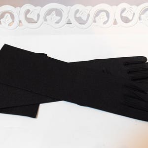 May include: A pair of long black satin gloves. The gloves are folded in half and laid out on a white surface.