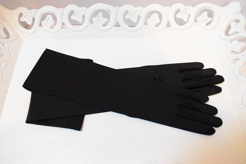 May include: A pair of long black satin gloves. The gloves are folded in half and laid out on a white surface.