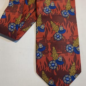 May include: A red necktie with a repeating pattern of fire hydrants, fire helmets, and fire trucks. The fire hydrants are gold, the helmets are blue, and the trucks are brown. The background features a flame design.