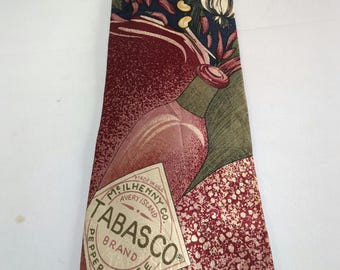Może przedstawiać: Czerwono-zielony krawat z jedwabiu z powtarzającym się wzorem papryczek chili, czosnku i butelki sosu Tabasco. Etykieta na butelce głosi "Made in USA, McIlhenny Co., Avery Island, Tabasco Brand Pepper Sauce, 2 fl oz."