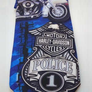 May include: Blue necktie featuring a motorcycle graphic and the Harley-Davidson Cycles logo. The tie also displays a police badge with the number 1. The background has a blue and white pattern.