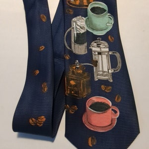 May include: A navy blue tie with a coffee theme. The tie features a coffee grinder, a french press, and three cups of coffee with coffee beans scattered around.