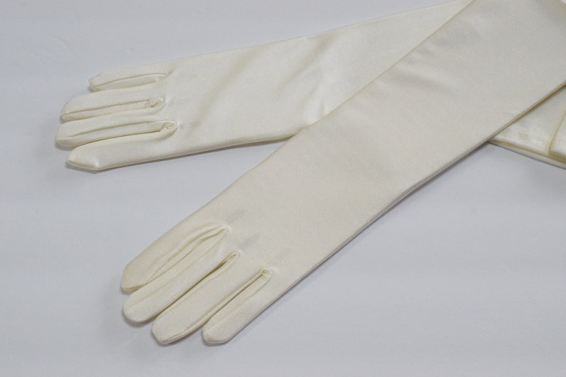 Puede incluir: Un par de guantes largos de sat&eacute;n blanco. Los guantes est&aacute;n completamente extendidos y los dedos est&aacute;n extendidos.
