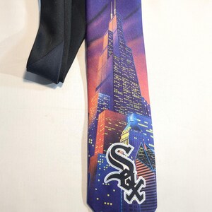 May include: A necktie featuring a cityscape design with the Chicago White Sox logo. The tie has a black backing and a vibrant illustration of buildings under a night sky with a full moon. The White Sox logo is prominently displayed.