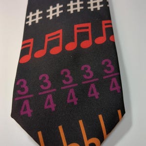 May include: Black necktie with a musical theme. The tie features colorful musical notes, treble clefs, and time signatures in shades of red, blue, green, and orange. The background is black.