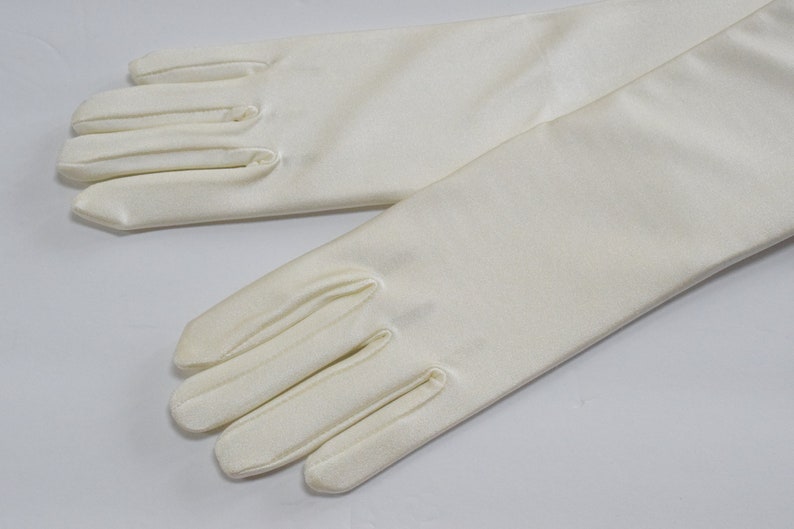Puede incluir: Un par de guantes largos de sat&eacute;n blanco. Los guantes son lisos y tienen una textura sedosa.