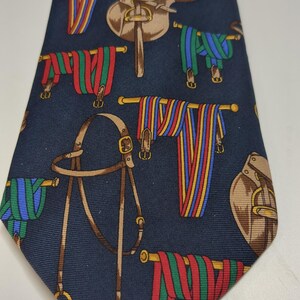 May include: A dark blue silk tie with a repeating pattern of brown saddles, bridles, and colorful striped ribbons.