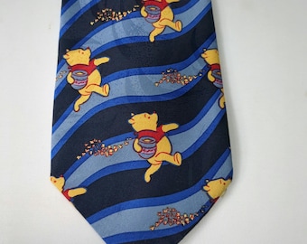 Könnte beinhalten: Eine blaue Krawatte mit einem sich wiederholenden Muster von Winnie-the-Pooh-Figuren, die Honigtöpfe tragen. Die Krawatte hat abwechselnd blaue und marineblaue Streifen mit kleinen Clustern aus roten und braunen Details.