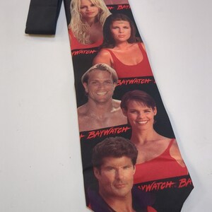 May include: Black necktie featuring images of Baywatch cast members. The tie has a black background with red text that reads "Baywatch". The tie is a classic accessory for fans of the television show.