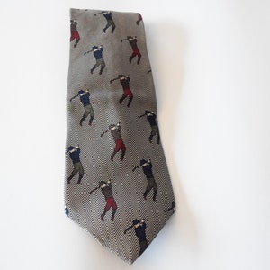 May include: A gray and white patterned tie with a repeating pattern of golfers in various poses. The golfers are wearing blue, red, and green clothing.