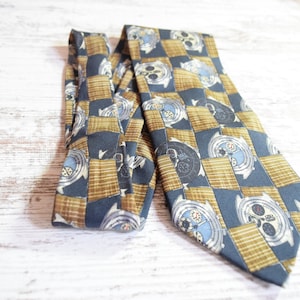 May include: A blue and gold patterned tie with a repeating design of watch faces. The tie is made of silk and has a classic design.