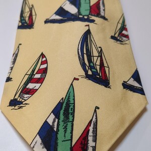 Puede incluir: Corbata amarilla con un estampado repetido de veleros. Los veleros tienen velas rojas, verdes, azules y blancas. La corbata está hecha de una tela suave y es adecuada para ocasiones formales o informales.
