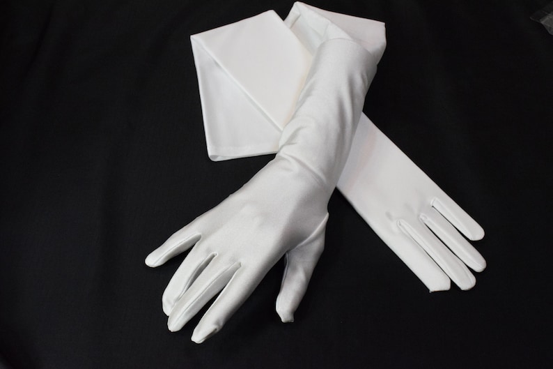 Puede incluir: Un par de guantes largos de sat&eacute;n blanco. Los guantes est&aacute;n doblados por la mitad y las puntas de los dedos son visibles.
