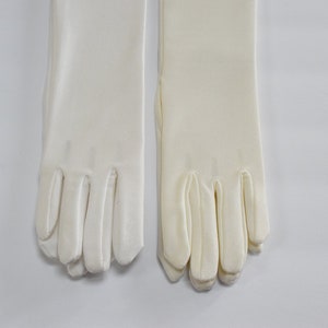 Puede incluir: Un par de guantes de sat&eacute;n blanco con dedos largos. Los guantes est&aacute;n hechos de una tela suave y lisa y tienen un dise&ntilde;o cl&aacute;sico.