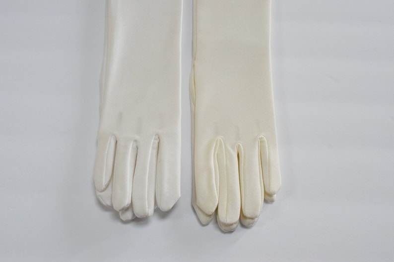 Puede incluir: Un par de guantes de sat&eacute;n blanco con dedos largos. Los guantes est&aacute;n hechos de una tela suave y lisa y tienen un dise&ntilde;o cl&aacute;sico.