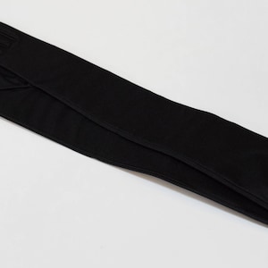 May include: A pair of long black gloves made of a smooth fabric. The gloves are folded in half and the fingertips are touching.