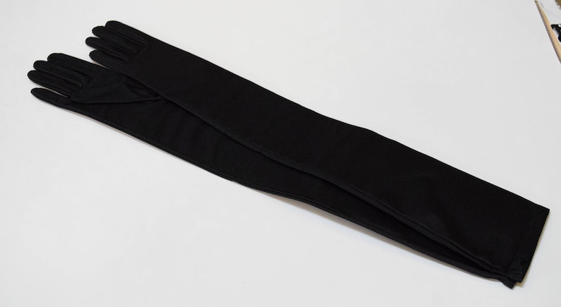 May include: A pair of long black gloves made of a smooth fabric. The gloves are folded in half and the fingertips are touching.