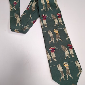 Puede incluir: Una corbata de seda verde con un patrón repetido de golfistas en varias poses. Los golfistas llevan camisas a rayas en rojo, azul, amarillo y blanco.