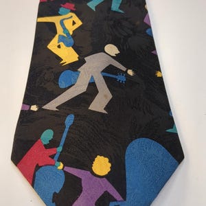 Peut inclure: Une cravate noire avec un motif répété de personnages colorés jouant d'instruments de musique. Les personnages sont dans des tons de rouge, jaune, bleu, violet et gris. La cravate a une extrémité pointue et une surface texturée.