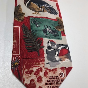 Pode incluir: Uma gravata vermelha e bege com um padrão de patos, samambaias e selos de caça. Os selos apresentam imagens de patos e o texto "Hunting Stamp - 1964-65" e "Department of the Interior".