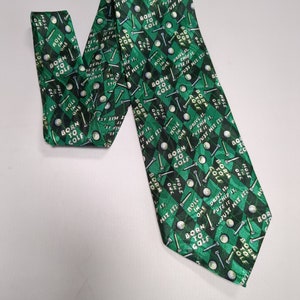 May include: A green necktie with a repeating pattern of golf balls, golf clubs, and the text "Born to Golf" in white and yellow lettering.