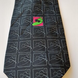 May include: Black necktie with a repeating pattern of a cartoon pickle wearing sunglasses. The tie has a square pattern with a single pickle wearing sunglasses in a pink square. A fun and unique accessory.