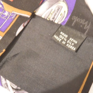 Puede incluir: Una corbata de seda negra con un patr&oacute;n colorido de im&aacute;genes relacionadas con el golf, incluyendo pelotas de golf, palos de golf y las palabras "Top-Flight". La corbata tiene una etiqueta que dice "Hand Sewn 100% Silk Made in Korea."