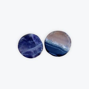 May include: Two round, polished stones. One is a deep blue with white veining. The other features a gradient of colors, including brown, blue, and green. The stones have a smooth, reflective surface and are set against a white background.