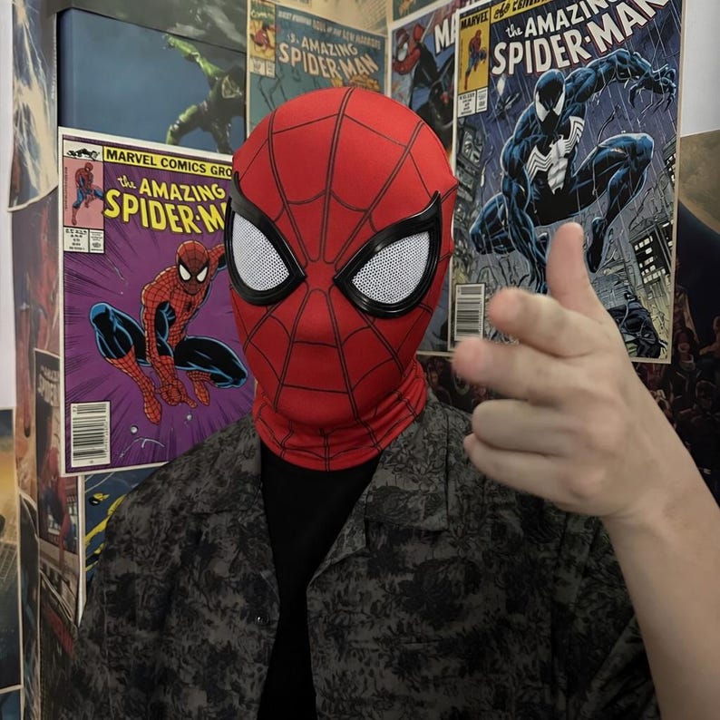 Puede incluir: Una m&aacute;scara roja de Spider-Man con telara&ntilde;as negras y malla blanca para los ojos. La m&aacute;scara cubre toda la cabeza y el cuello. En el fondo se ven portadas de c&oacute;mics de Spider-Man.