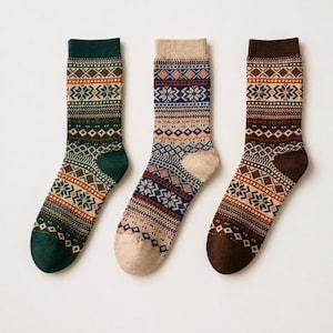 May include: Three pairs of crew socks featuring intricate Fair Isle patterns. The first sock is dark green, the second is beige, and the third is dark brown. Each sock displays a repeating design of snowflakes, diamonds, and horizontal stripes.