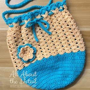 May include: A crocheted drawstring bag with a peach and turquoise color scheme. The bag has a flower embellishment and a long turquoise strap.