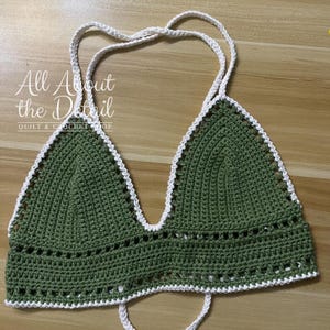 May include: Green crochet bikini top with white trim. The top has a halter style with adjustable straps.  "All About the Detail Quilt & Crochet Shop" is printed on the image.