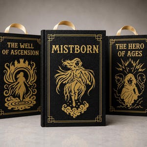 Puede incluir: Tres libros de tapa dura con cubiertas negras y letras e ilustraciones doradas. Los títulos son "The Well of Ascension", "Mistborn" y "The Hero of Ages". Cada libro tiene un asa de cinta dorada.