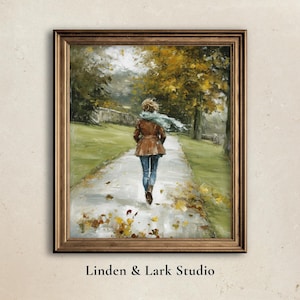 May include: An oil painting in a gold frame depicts a person walking away on a path through a park in autumn. The person wears a brown coat, blue jeans, and a blue scarf. Fallen leaves are scattered on the path.