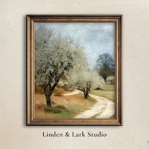 May include: A framed landscape painting featuring a dirt road winding through a field of trees with white blossoms. The artwork has a vintage aesthetic, with a gold-colored frame and the text "Linden & Lark Studio" at the bottom.